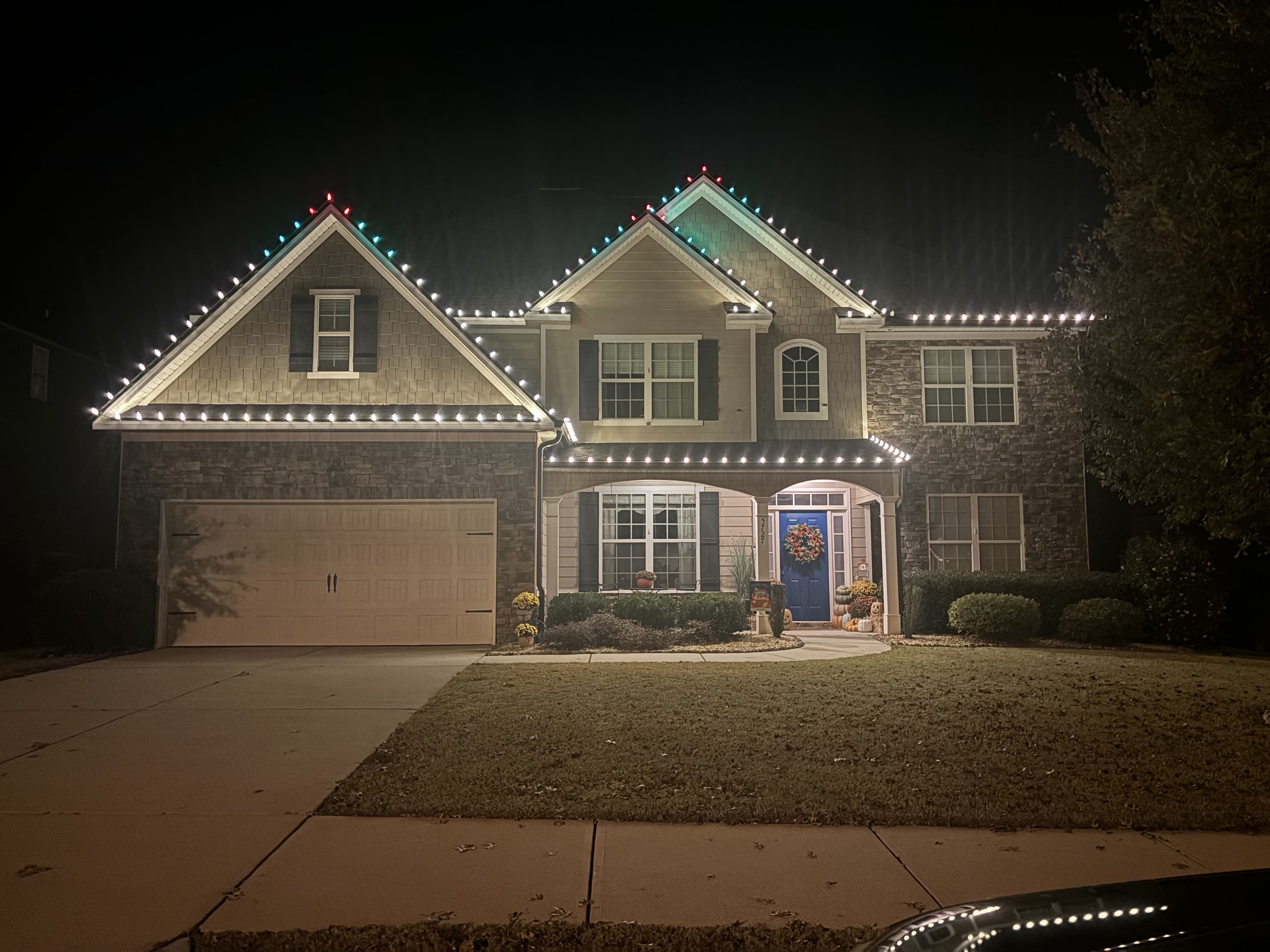 Decorated home with festive lights and wreath, glowing at night during the holiday season.