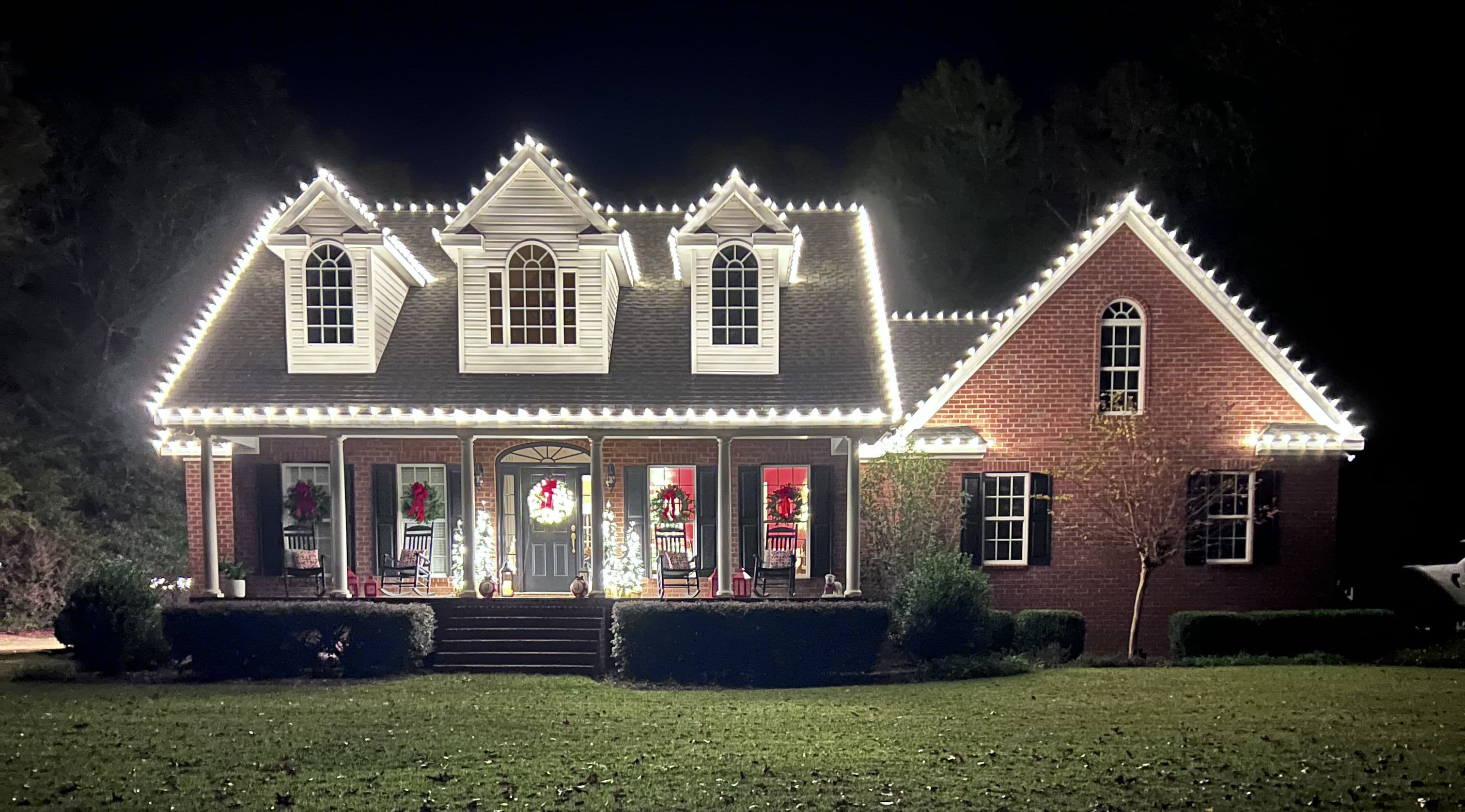 Elegant brick house adorned with festive holiday lights and decorations at night.